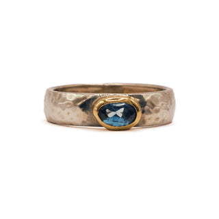 A unique blend of the rustic and the resplendent, this band of hammered sterling silver showcases a sparkling cut of brilliant blue topaz in a 14 karat yellow gold bezel. 